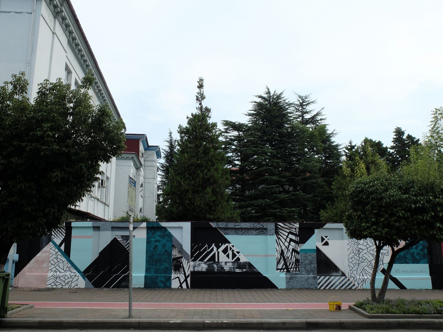 Na zdjęciu widać fragment ulicy w miejscowości Batumi (Gruzja). Wzdłuż ulicy znajduje się ok dwumetrowy mur, na którym znajduje się graffiti przedstawiające nieregularne figury geometryczne, paski, załamania.