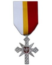Zdjęcie srebrnej Odznaki Honorowej Województwa Małopolskiego - Krzyż Małopolski. Odznaka przedstawia krzyż na Giewoncie zawieszony na wstążce w kolorach białym złotym i czerwonym symbolizującym flagę Małopolski.