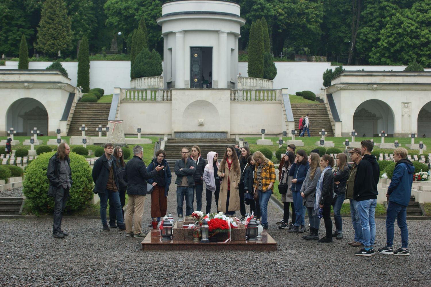 Duża grupa osób stojąca przed tablicą pamiątkową na Cmentarzu Łyczakowskim. W tle groby.