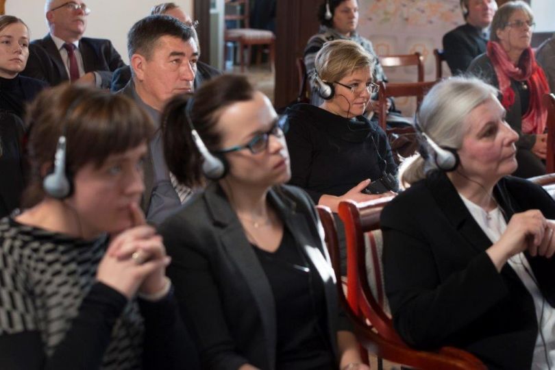 Zdjęcie przedstawia grupę osób ze słuchawkami na głowach słuchających wykładu